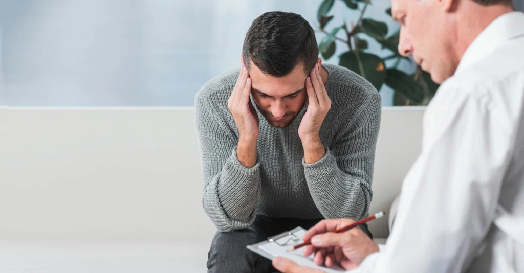 Man holding his head while a doctor takes notes