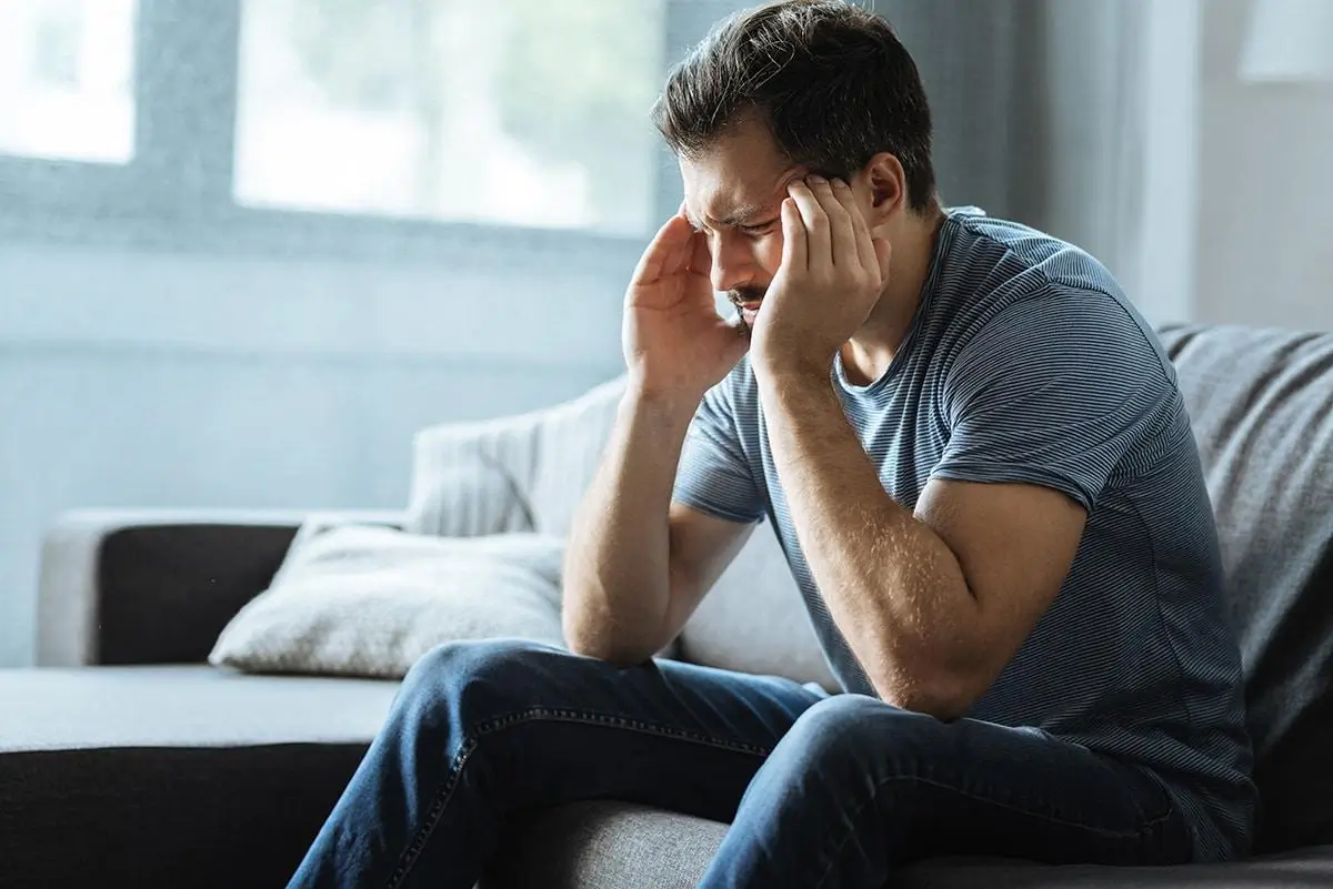 Man holding his head while sitting on a couch