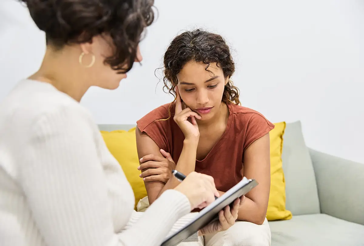 Counselor sitting beside a pensive young woman on a couch