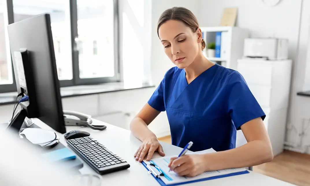 Nurse filling out paperwork at a computer workstation