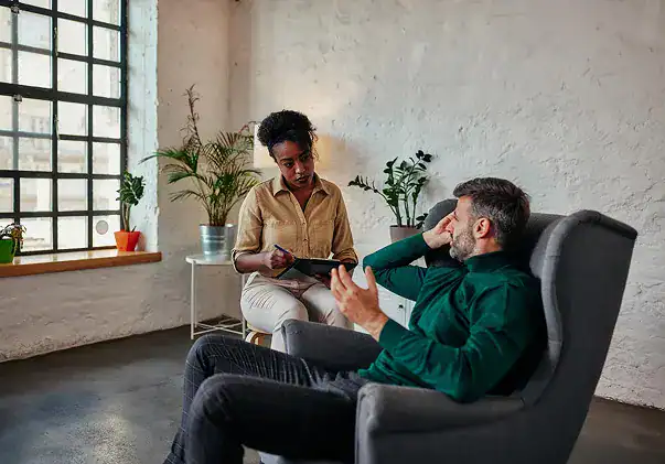 Therapist taking notes during a session with a man in an armchair