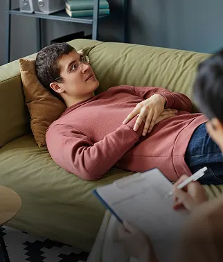 Client lying on a couch during a therapy session while the therapist takes notes
