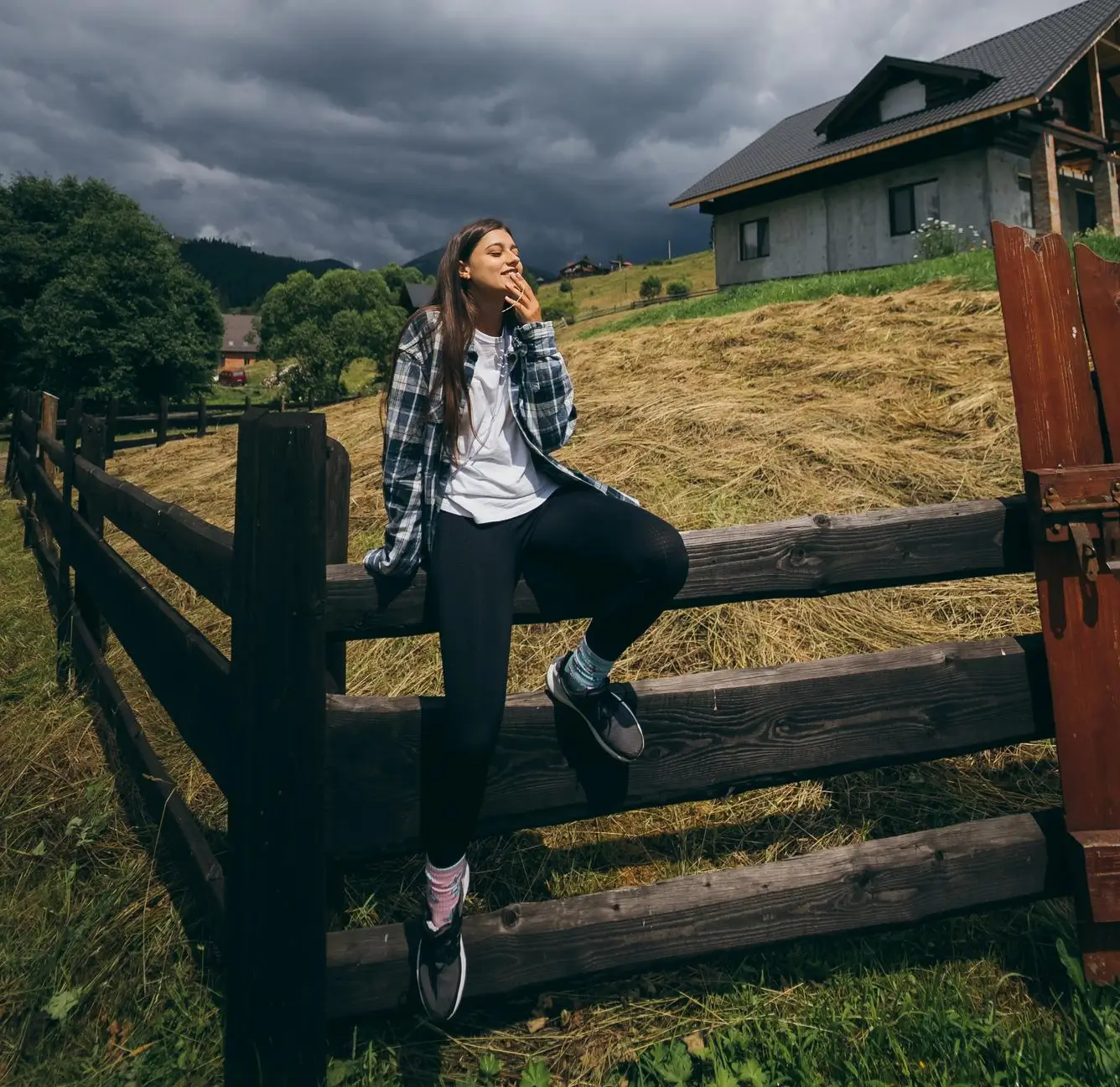 Woman sitting on a wooden fence at a rural property under a cloudy sky
