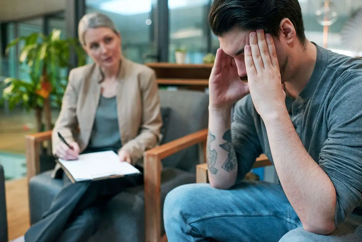Counselor taking notes while a man holds his head in distress