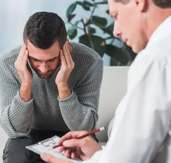 Man holding his head while a counselor writes notes