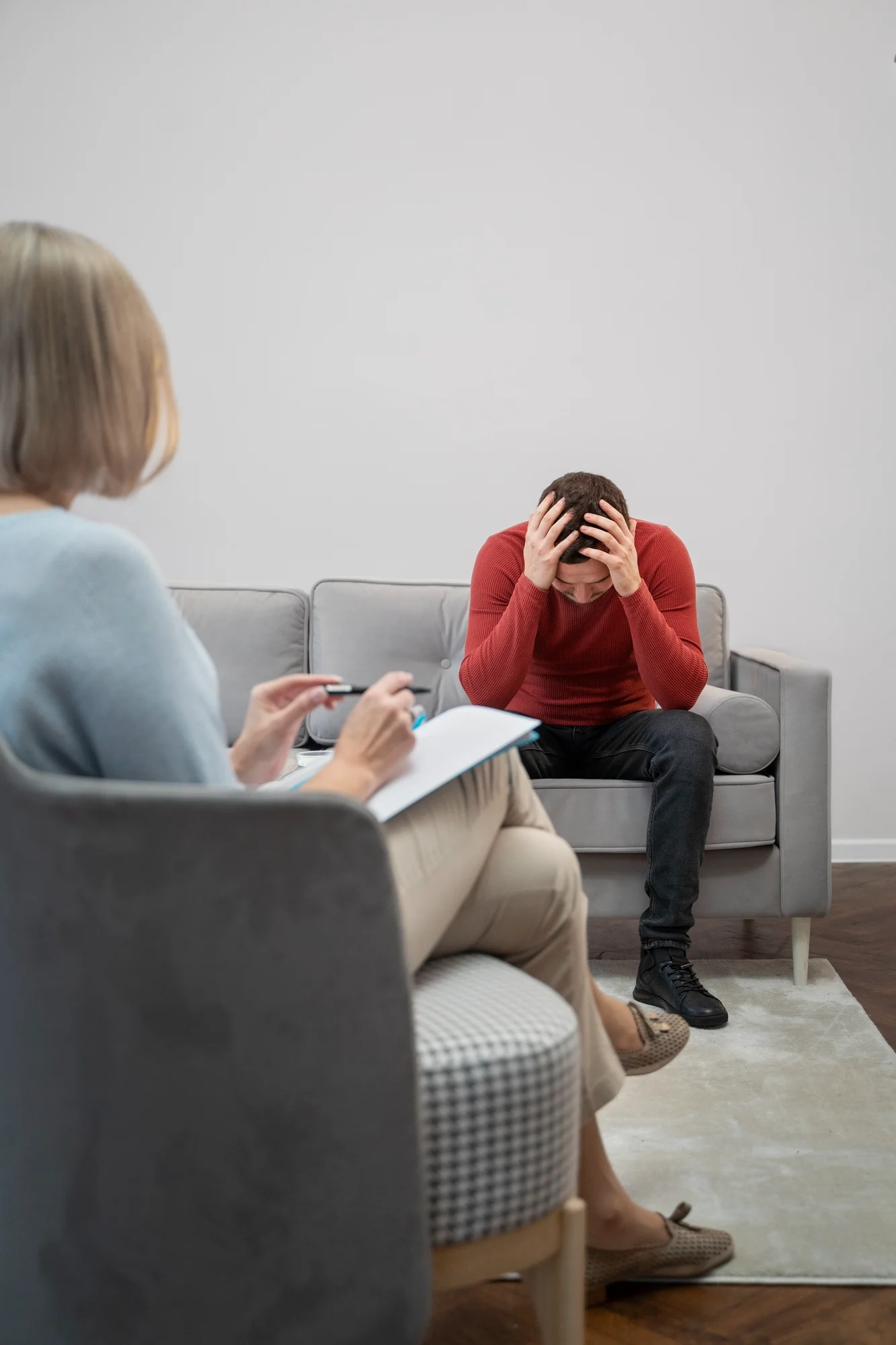 Therapist taking notes while a distressed man holds his head