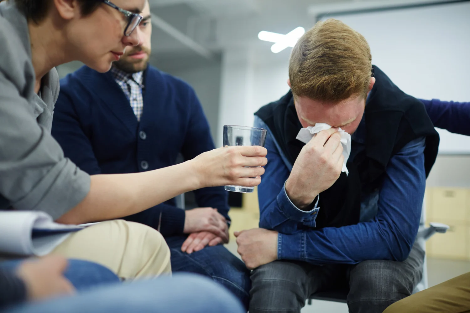 Group members comforting a tearful man at a support meeting