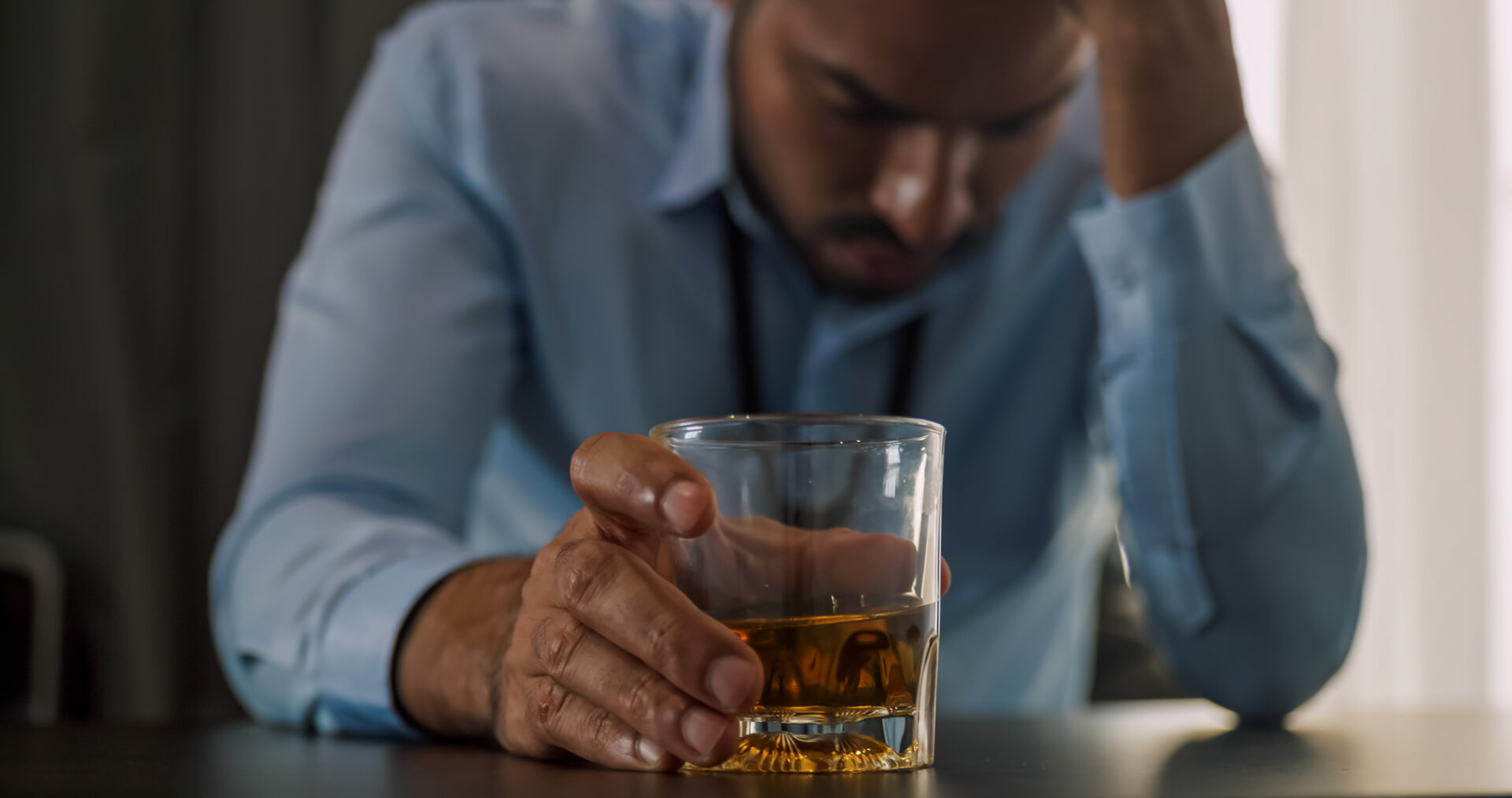 A man drinking holding a glass of alcohol wondering "does outpatient alcohol rehab work?"