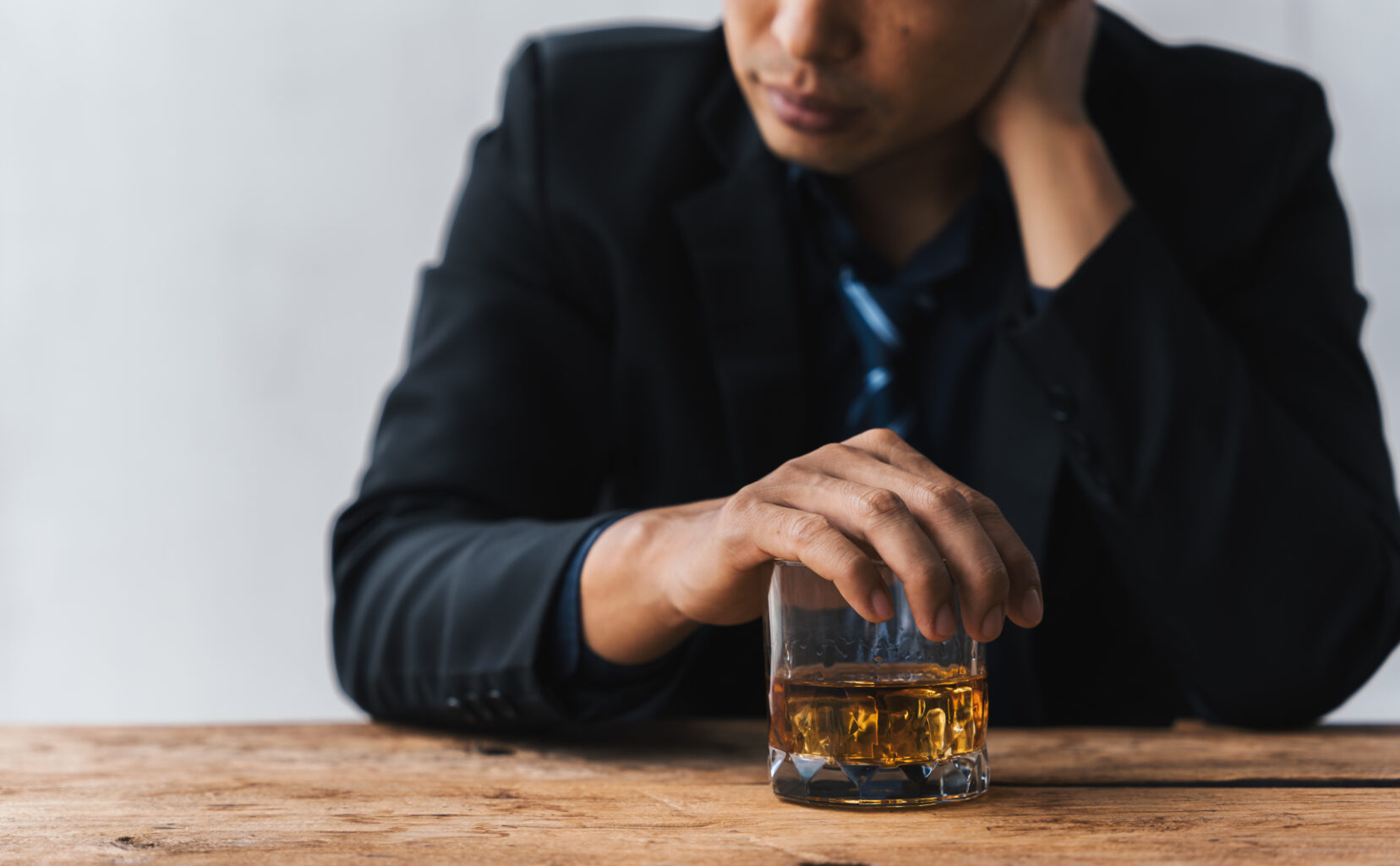 A man sitting with his hand over a glass of alcohol.