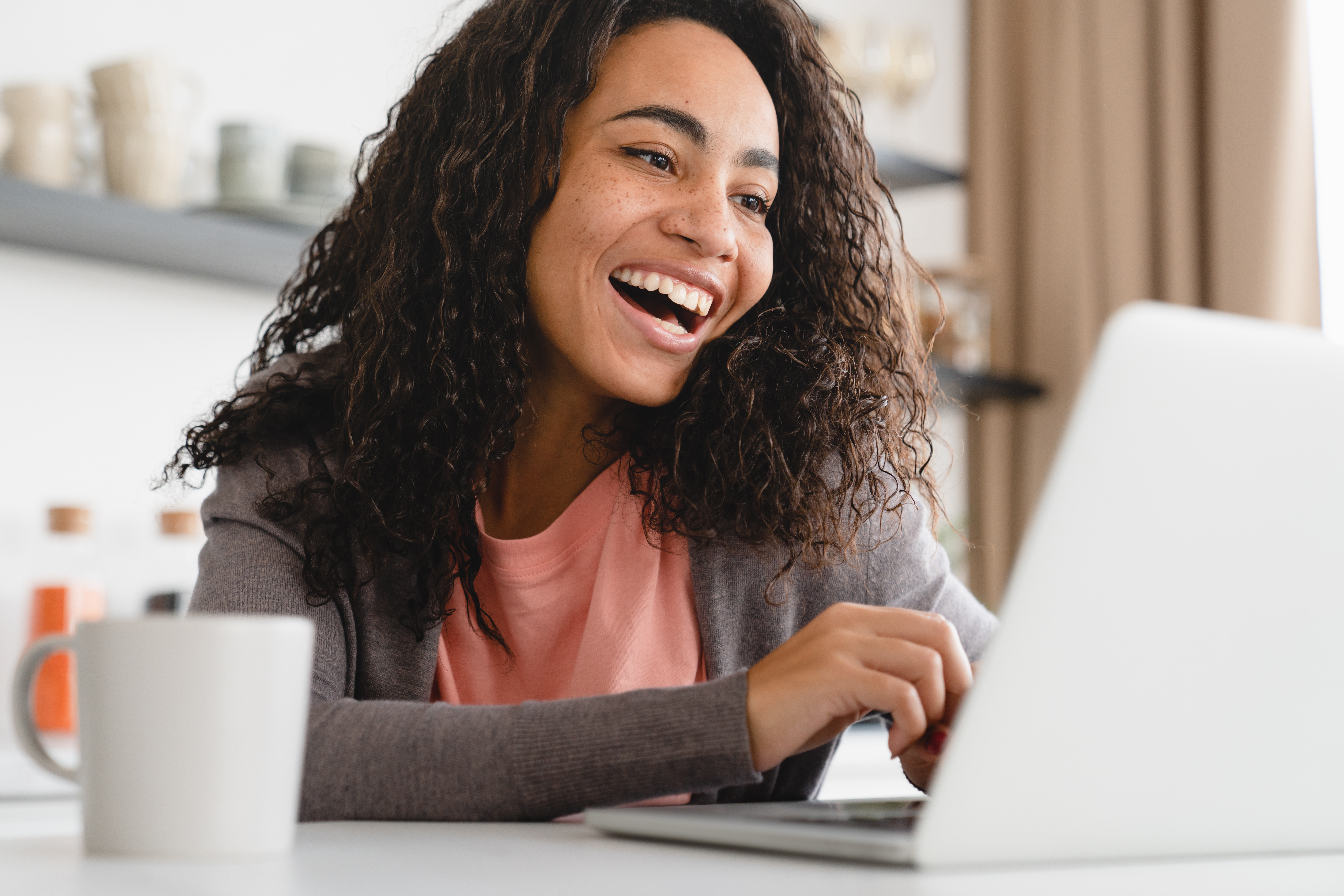 A woman smiling at her computer while exploring online iop programs.
