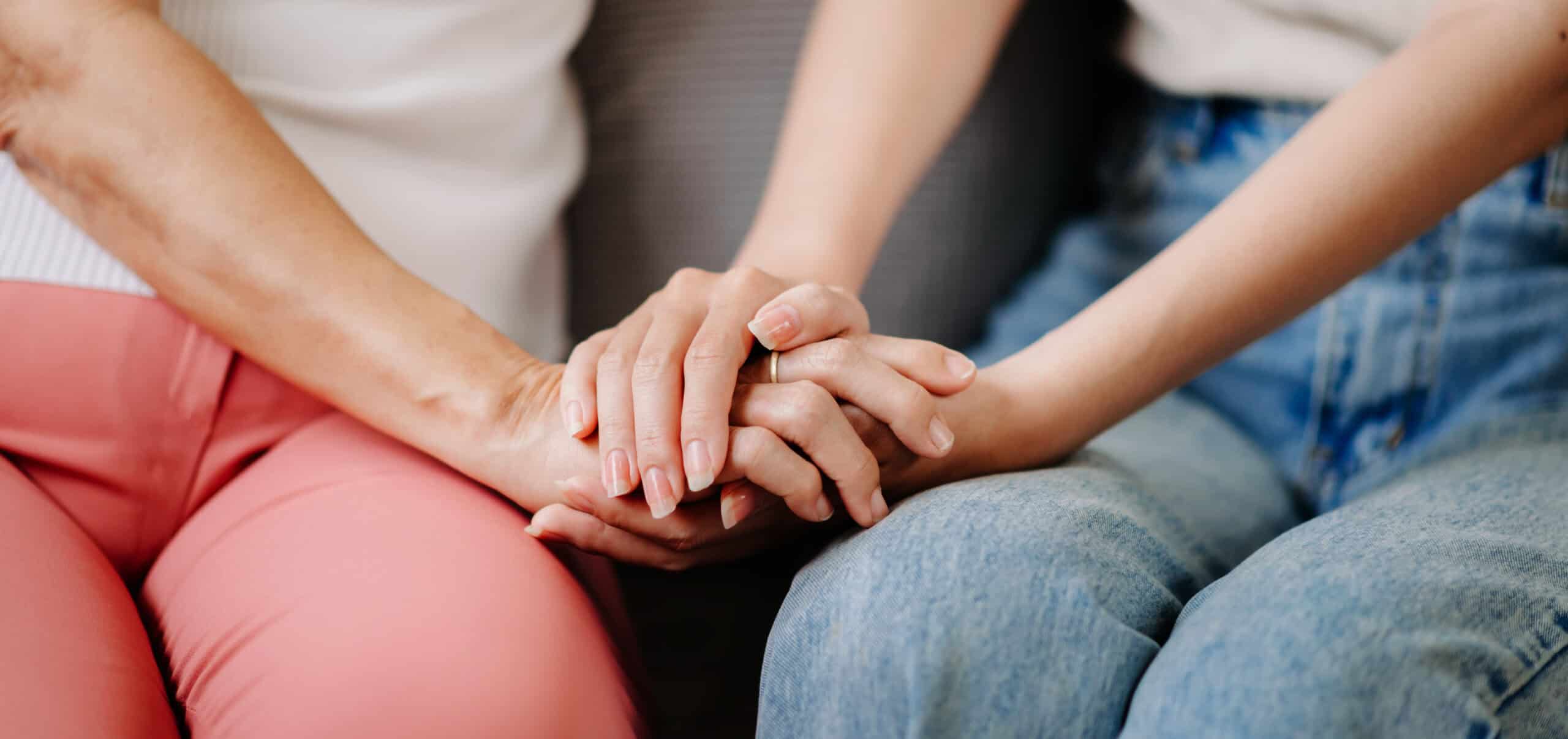 A close-up of two people holding hands during a supportive conversation.