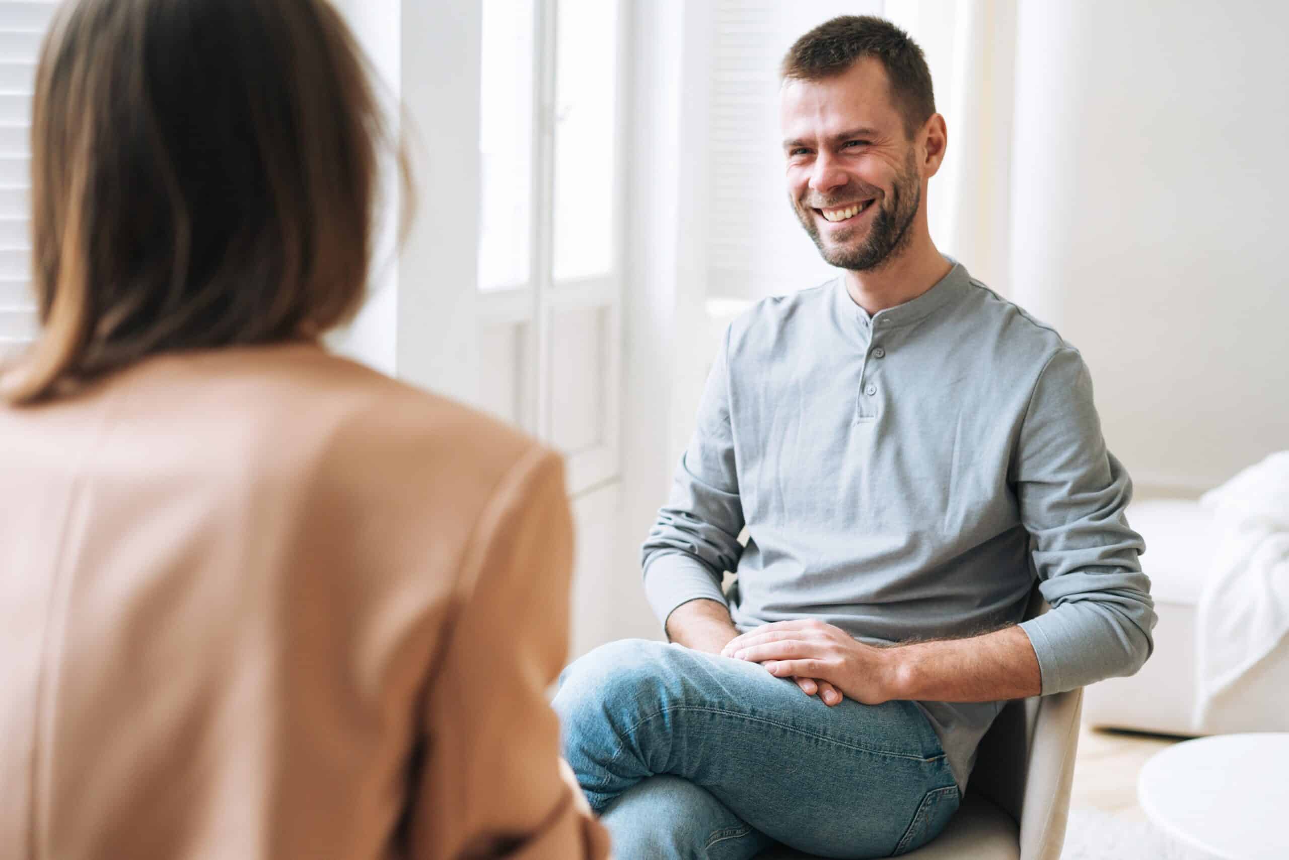 A man smiling in a therapy session while speaking about his mental health.